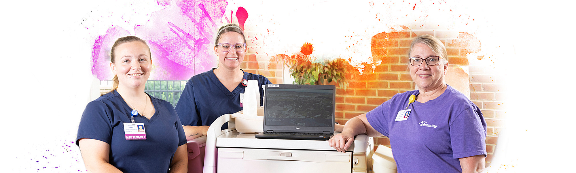 Three female healthcare employees standing by a cart with a laptop